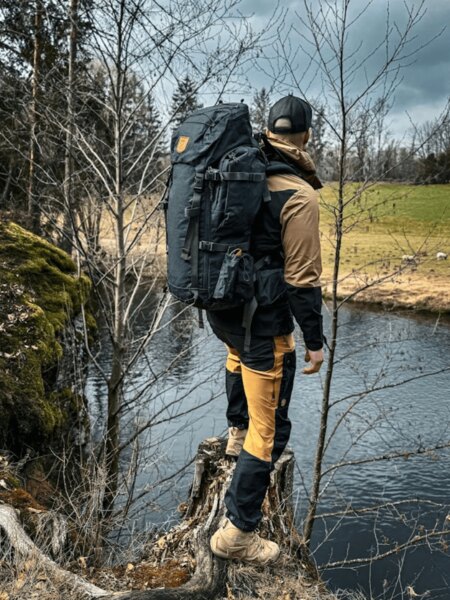 Outdoorové nohavice Fjällräven a batoh pri riečnom brehu v prírode. Foto: Rigad