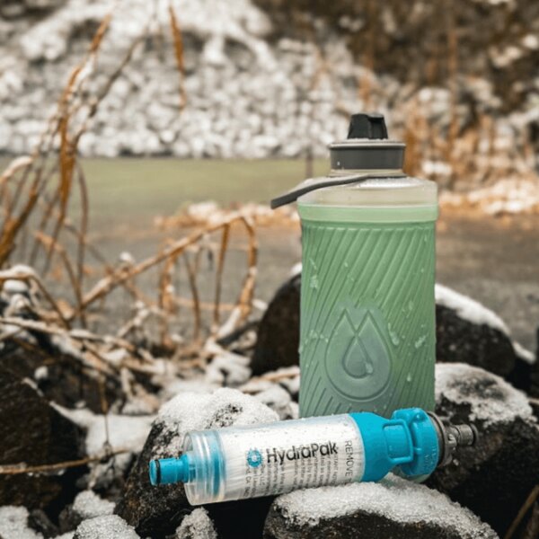 Hydrapak fľaša a vodný filter položené na snehu. Outdoor hydratačný systém v zimnom prostredí. Foto: Rigad
