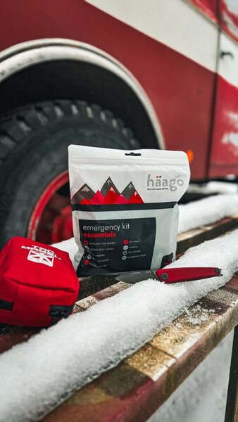 Núdzová zimná súprava Haago s termofóliou a ohrievačmi rúk položená v snehu pred vozidlom – praktická výbava do auta pre zimnú sezónu 2025/26. Foto: Rigad