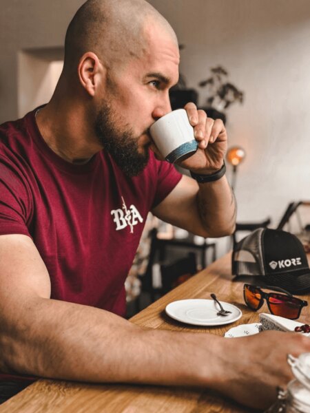 Muž s taktickým vzhľadom pri káve – detail na tričko BfA a čiapku Kore Essentials. Foto: Rigad