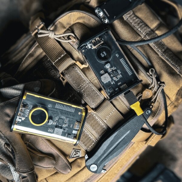 Powerbanka C4 Explosive Tactical<sup>&reg;</sup>, 9600 mAh, položená na taktickom výstroju; transparentné telo s displejom, rýchle nabíjanie a robustný dizajn do terénu. Foto: Rigad