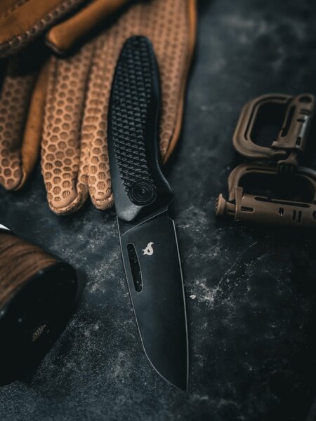 Moderný zatvárací nôž Black Fox<sup>&reg;</sup> s čiernou čepeľou položený na pracovnej rukavici. Foto: Rigad