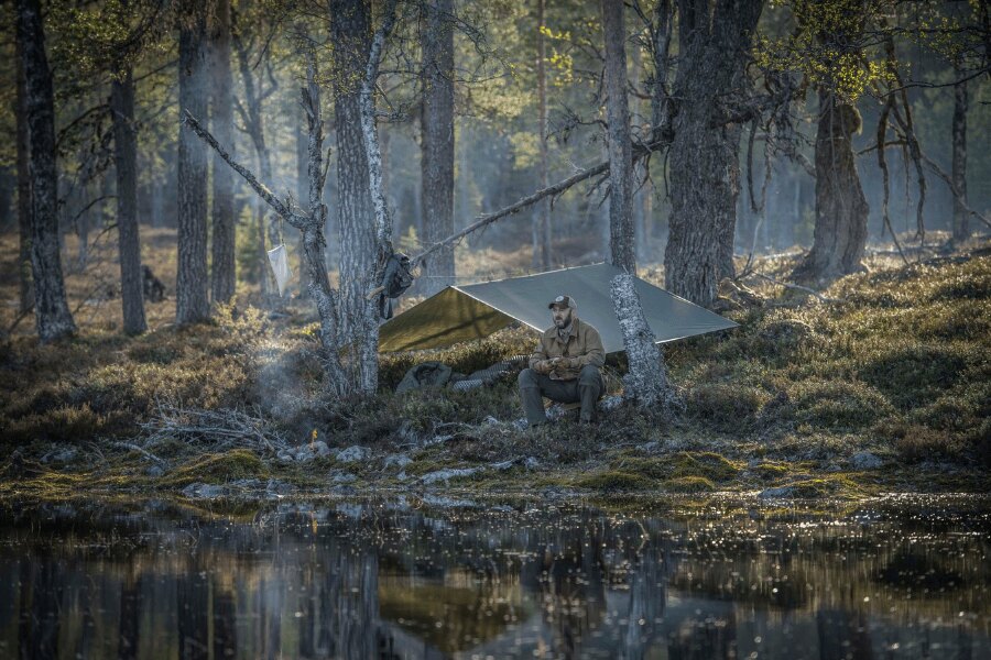Nízkoprofilový tábor — tarp v zemitých farbách splynie s okolím, oheň malý a krytý. Odchod = LNT: miesto zarovnať, žiadne stopy. Foto: Helikon-Tex, Rigad