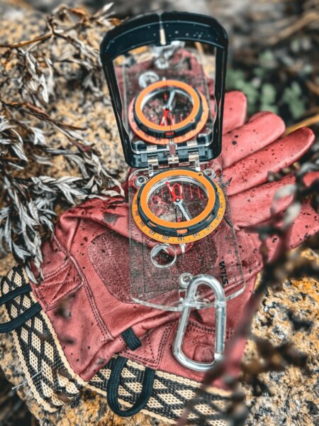 Kompas a rukavice položené v teréne – navigácia v prírode bez GPS pomocou buzoly. Foto: Rigad