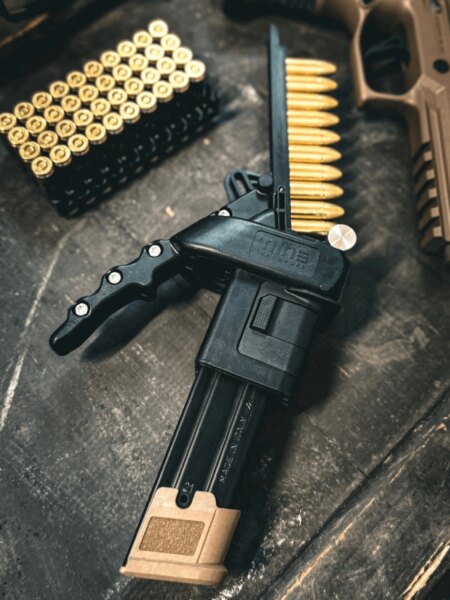 Nabíjač zásobníkov Nine Reloaded vedľa nábojov kalibru 9 mm Luger a pištole.