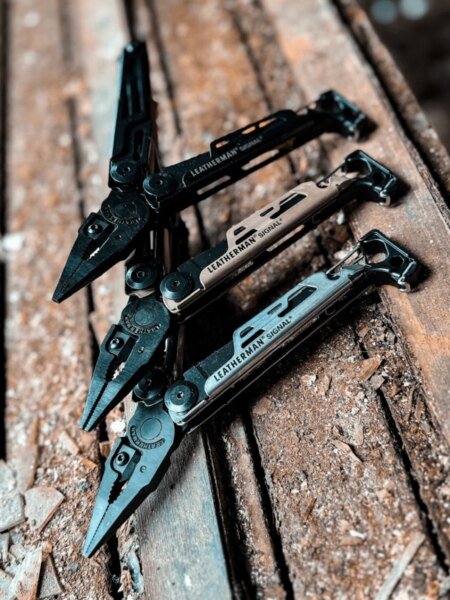 Tri multitooly Leatherman Signal v rôznych farebných prevedeniach položené na drevenom povrchu.