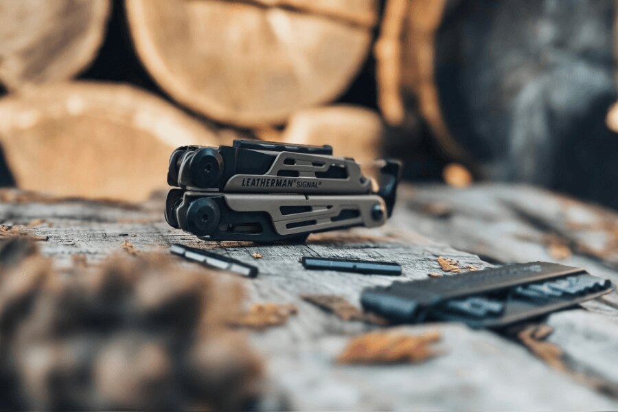 Leatherman Signal položený na drevenom stole s bitmi a príslušenstvom v outdoorovom prostredí.