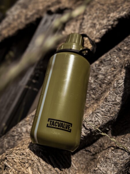 Polná fľaša TacValve<sup>®</sup> ModCan v zelenom prevedení položená na drevenom podklade v outdoorovom prostredí.