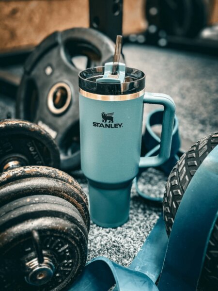 Termohrnček Stanley so slamkou položený medzi činkami a fitness vybavením.