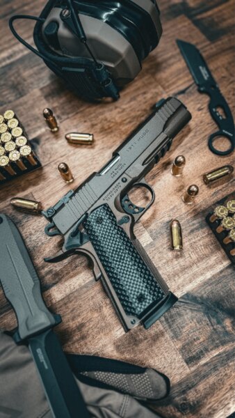 Pištoľ Schmeisser HUGO 1911 5" v kalibri .45 ACP položená na stole so strelivom a streleckým vybavením.
