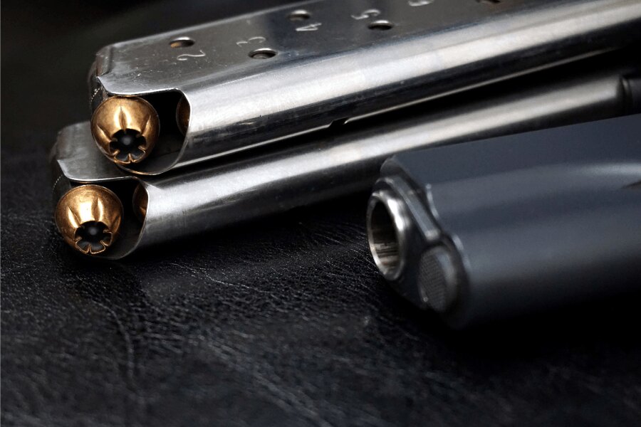 Detail zásobníkov pištole M1911 s nábojmi .45 ACP a časťou pištole v pozadí.