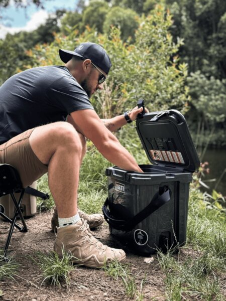 Muž otvára transportný box YETI LoadOut GoBox pri pobyte pri vode.