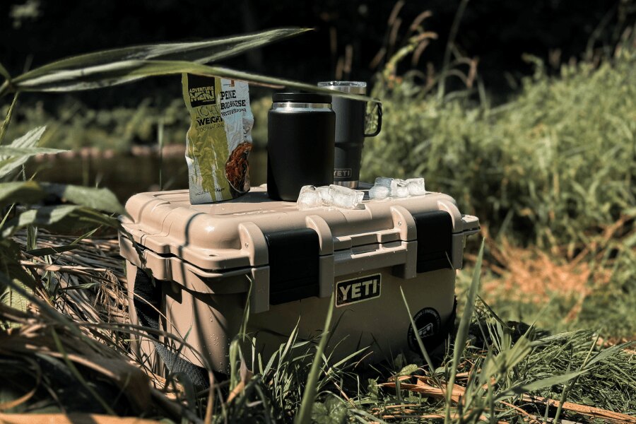 Transportný box YETI LoadOut GoBox s baleným jedlom a termohrnčekmi v prírode.