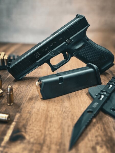 Pištoľ Glock 17 Gen5 s mechanickými mieridlami položená na stole so zásobníkom, strelivom a nožom.