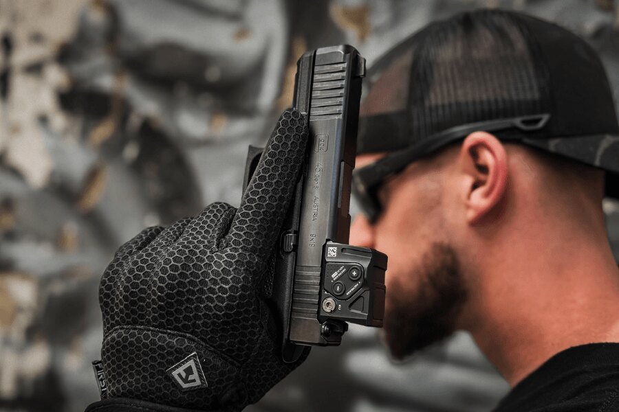 Detail pištole Glock 45 s kolimátorom držanej v rukavici.