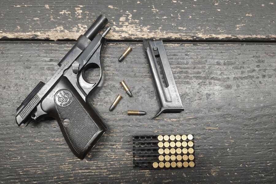 Pištoľ Beretta 71 s vybratým zásobníkom a nábojmi .22 LR na tmavom drevenom stole.