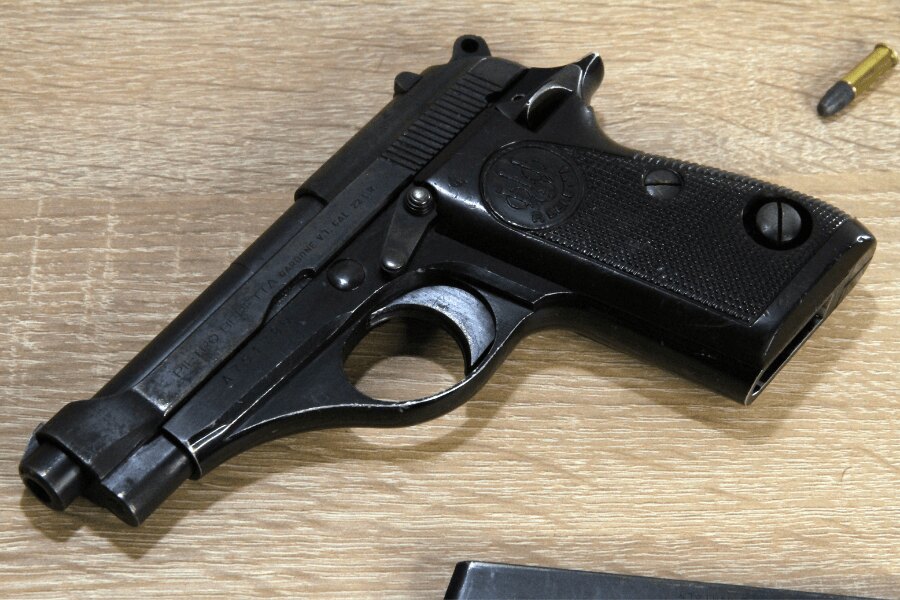 Detail pištole Beretta 71 položenej na svetlom drevenom stole.