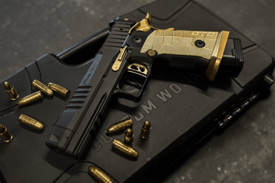 Pištoľ SIG Sauer P211-GTO SPECTRE COMP v čiernozlatom prevedení, položená na prepravnom kufri medzi nábojmi.