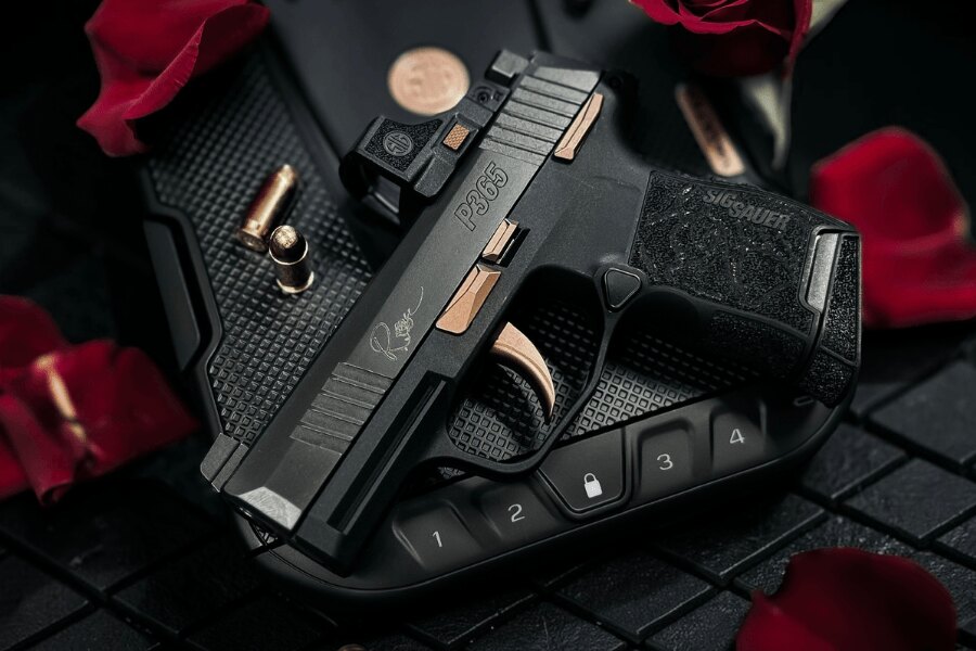 Pištoľ SIG Sauer P365 ROSE s kolimátorom a ružovo zlatými prvkami na uzamykateľnom boxe medzi okvetnými lístkami ruží.