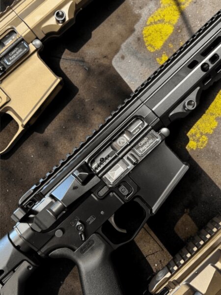 Tri pušky platformy AR-15 v čiernom a pieskovom prevedení položené vedľa seba na betónovom povrchu.